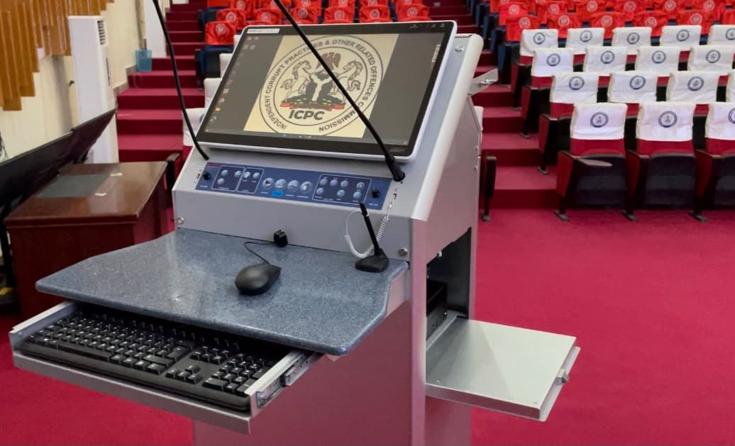 Multimedia lectern with a touchscreen display, gooseneck microphones and a control panel facing rows of auditorium seats